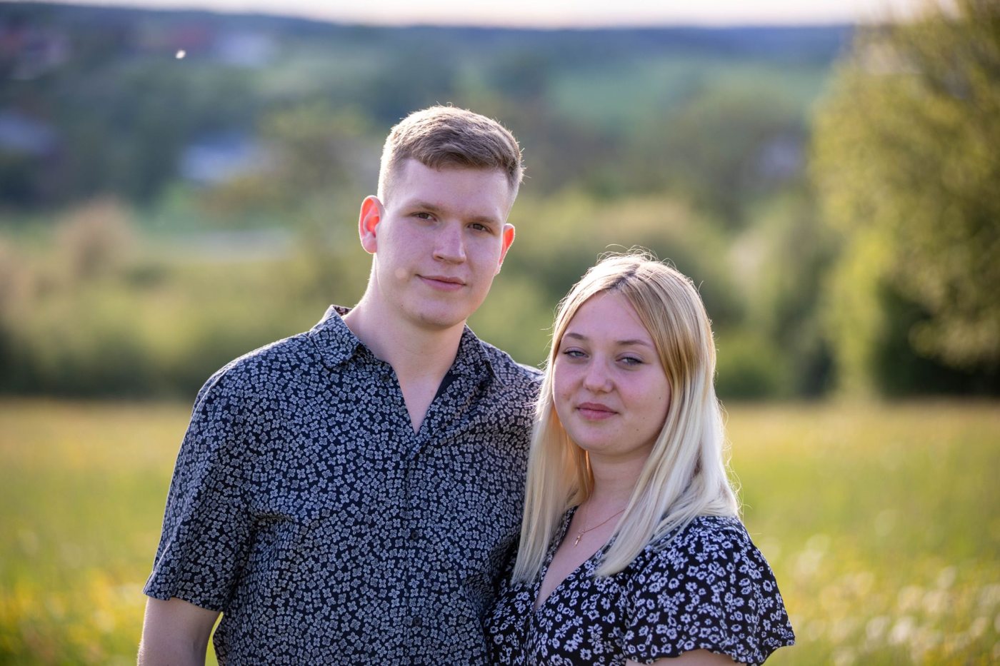 Junges Paar steht im warmen Abendlicht vor einer unscharfen hügeligen Landschaft