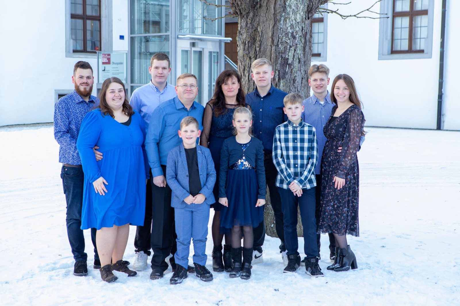 Große Familie in Blautönen steht im Schnee vor einem alten Baum im Schlosshof