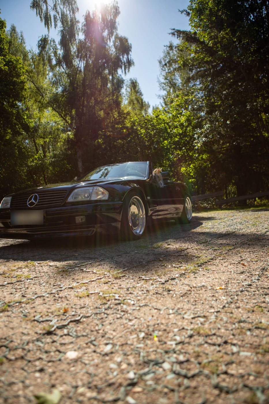 Schwarzes Cabrio mit Blumenschmuck auf einem Schotterplatz im Gegenlicht
